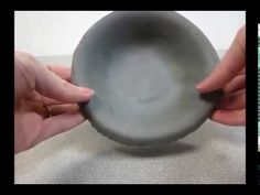 two hands holding a gray bowl on top of a table