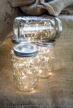 two mason jars sitting on top of a burlock covered tablecloth with lights in them