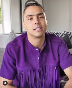 a man in a purple shirt sitting on a couch with his eyes closed and one eye open