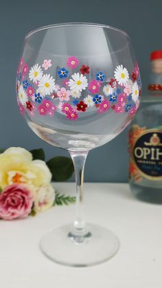 a wine glass with flowers painted on the side and a bottle in the back ground