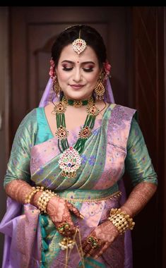 a woman in a purple and green sari with jewelry on her hands, looking down at the camera