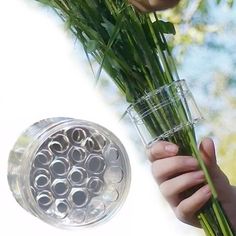 a person holding some flowers in front of a glass vase with water on it and another hand holding the stems