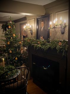 a christmas tree in front of a fireplace with candles on it and a man's portrait