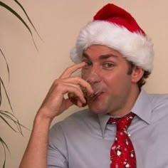 a man wearing a santa hat and drinking from a glass while talking on the phone