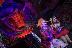 two women dressed as clowns sit in front of a spinning wheel on display at a carnival