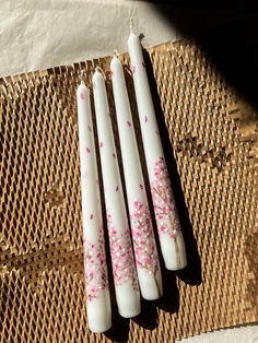 three white candles sitting on top of a woven place mat with pink flowers painted on them