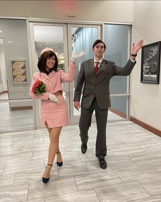 a man and woman dressed in business attire walking down a hall way with their hands up