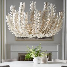 a white table topped with a vase filled with flowers next to a large wooden chandelier