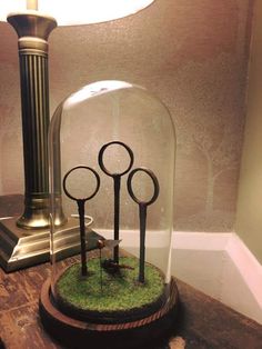 some scissors are under a glass dome on a wooden table next to a clock and lamp