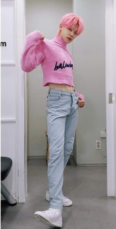 a girl with pink hair wearing a pink sweater and jeans standing in front of a white wall