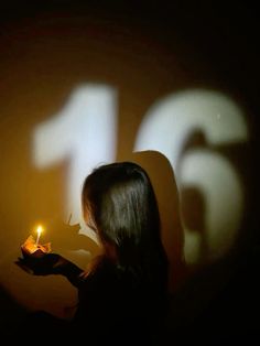 a woman holding a lit candle in front of the number fifteen six projected on a wall