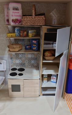 a dollhouse kitchen with an oven, refrigerator and shelves full of food on the floor