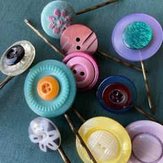 many different colored buttons and needles on a blue tablecloth with pins in the middle