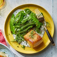 a yellow plate topped with green vegetables and fish on top of rice next to a fork