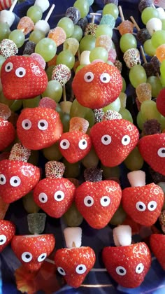 some fruit with eyes on them sitting in a blue bowl next to grapes and strawberries