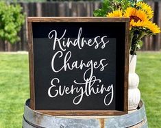 a sign that says kindness changes everything on it next to a vase with sunflowers