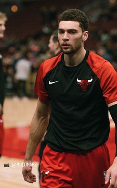 a man in red and black uniform standing on a basketball court with other people watching