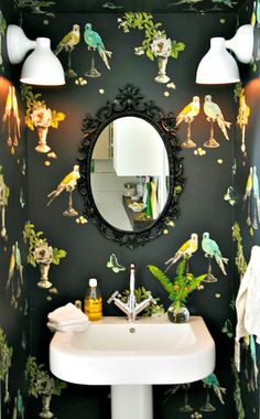 a bathroom sink sitting under a mirror next to a wallpapered wall with birds on it