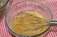 a glass bowl filled with liquid and whisk on top of a red checkered tablecloth