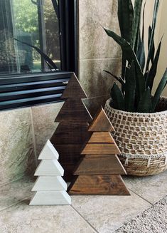 three wooden christmas trees sitting on top of a counter next to a potted plant