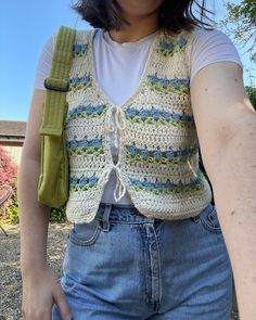 a woman wearing a crocheted vest and holding onto a green belted bag