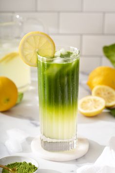 a tall glass filled with green liquid next to lemons and other ingredients on a table