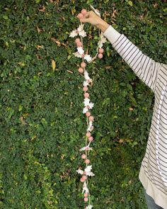 a person holding flowers in front of a green wall with vines and leaves on it