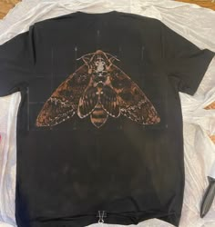 a black shirt with a brown moth on it sitting on top of a white sheet