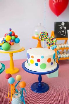 there is a birthday cake on the table with candy and balloons in the back ground