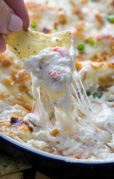 a person dipping a tortilla chip into a casserole dish with chicken and cheese