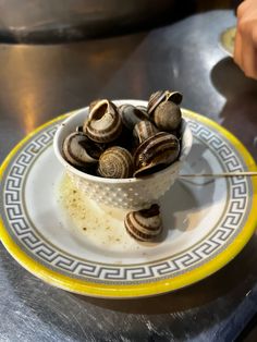 a bowl filled with snails sitting on top of a table next to a yellow and white plate