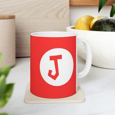 a red and white coffee mug sitting on top of a counter next to some fruit