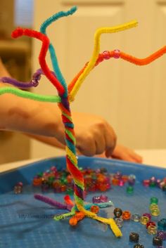 a child's hand is making a tree made out of beads and plasticine