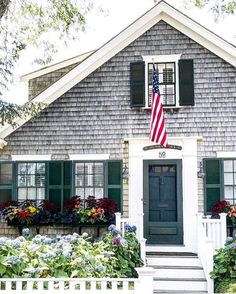 an american flag is hanging on the front door of a gray house with green shutters