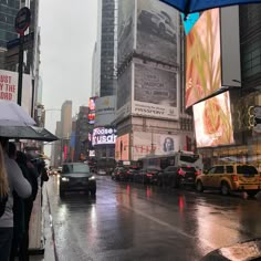 people are standing in the rain with umbrellas over their heads as cars pass by on a city street