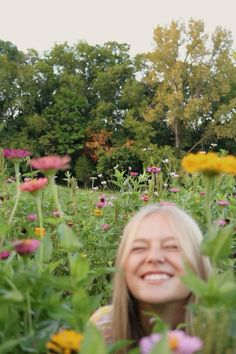 a woman standing in the middle of a field full of flowers smiling at the camera