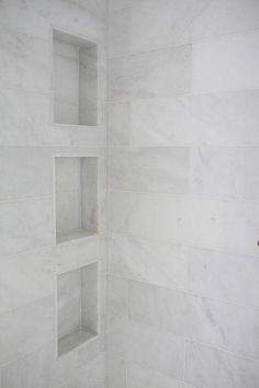 a white tiled shower with shelves in the corner and marble tiles on the wall behind it