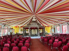 a large room filled with lots of red and white chairs under a ceiling covered in colorful draping