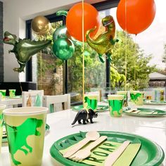 the table is set with green and orange plates, silverware, and dinosaur balloons