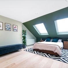 a bed sitting under two windows in a bedroom next to a blue couch and rug