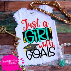 a white shirt with the words just a girl with goals on it and a gold necklace