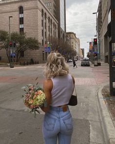 a woman is walking down the street with flowers in her hand and holding a bouquet