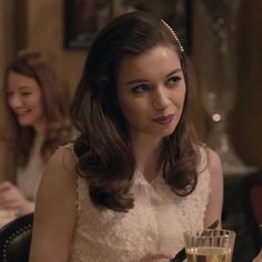 a woman sitting at a table with a glass of wine in front of her and another woman standing behind her