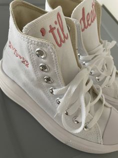 a pair of white high top sneakers with red lettering on the soles and laces