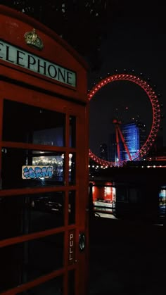 a red phone booth with the london eye in the background and lights on at night