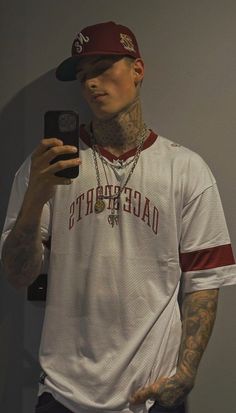 a tattooed man taking a selfie in front of a mirror with his cell phone