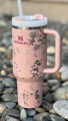 a pink mickey mouse travel mug with a straw in it sitting on some rocks and pebbles