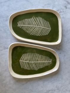 two green trays with white designs on them sitting on a marble counter top next to each other