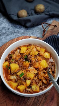 a white bowl filled with stew and potatoes on top of a wooden cutting board next to two spoons