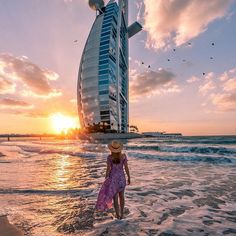 a woman standing in the ocean next to a tall burj building at sunset